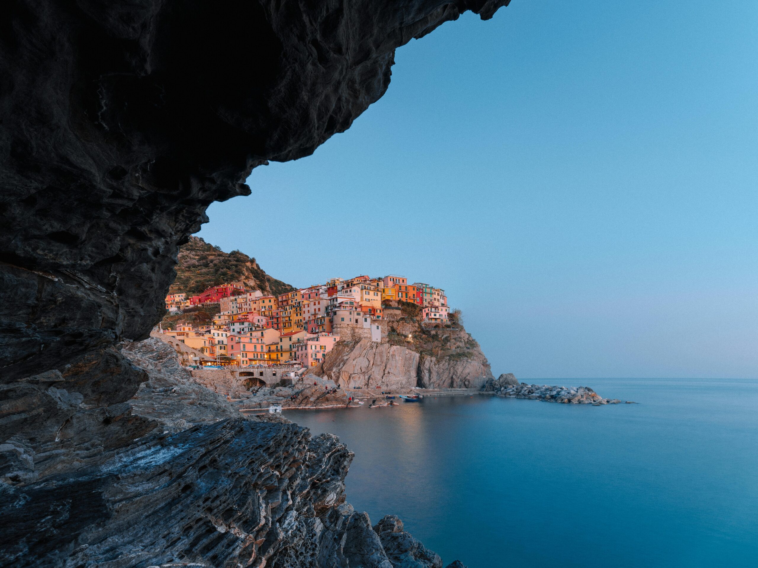 Stunning view of Manarola's colorful cliffs and calm sea under a blue evening sky.